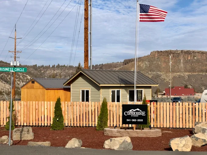Large fifth wheel on paved site with trees and canyon rimrock in background